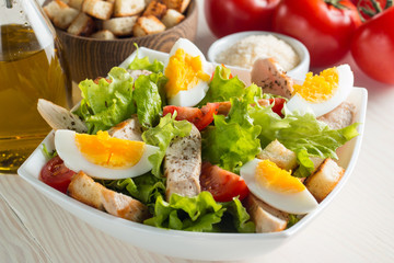 Fresh Caesar salad with delicious chicken breast, ruccola, spinach, cabbage, arugula, egg, parmesan and cherry tomato on wooden background. Oil, salt and pepper. Healthy and diet food concept.