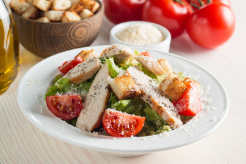 Fresh salad with delicious chicken breast, ruccola, spinach, cabbage, arugula and tomato on wooden background. Oil, salt and pepper.