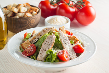 Fresh salad with delicious chicken breast, ruccola, spinach, cabbage, arugula and tomato on wooden background. Oil, salt and pepper.