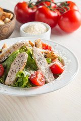 Fresh salad with delicious chicken breast, ruccola, spinach, cabbage, arugula and tomato on wooden background. Oil, salt and pepper.