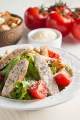 Fresh salad with delicious chicken breast, ruccola, spinach, cabbage, arugula and tomato on wooden background. Oil, salt and pepper.