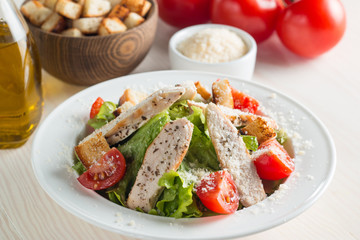 Fresh salad with delicious chicken breast, ruccola, spinach, cabbage, arugula and tomato on wooden background. Oil, salt and pepper.