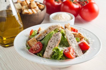 Fresh salad with delicious chicken breast, ruccola, spinach, cabbage, arugula and tomato on wooden background. Oil, salt and pepper.