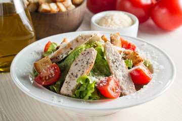 Fresh salad with delicious chicken breast, ruccola, spinach, cabbage, arugula and tomato on wooden background. Oil, salt and pepper.