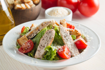 Fresh salad with delicious chicken breast, ruccola, spinach, cabbage, arugula and tomato on wooden background. Oil, salt and pepper.