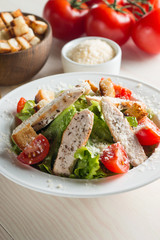 Fresh salad with delicious chicken breast, ruccola, spinach, cabbage, arugula and tomato on wooden background. Oil, salt and pepper.