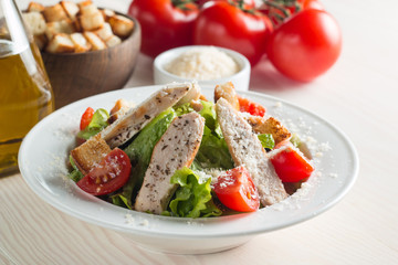 Fresh salad with delicious chicken breast, ruccola, spinach, cabbage, arugula and tomato on wooden background. Oil, salt and pepper.