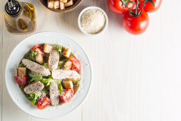 Fresh salad with delicious chicken breast, ruccola, spinach, cabbage, arugula and tomato on wooden background. Oil, salt and pepper.