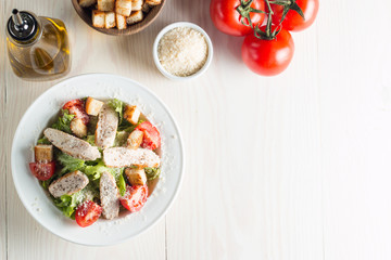 Fresh salad with delicious chicken breast, ruccola, spinach, cabbage, arugula and tomato on wooden background. Oil, salt and pepper.