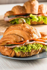 Photo of tasty and fresh croissant sandwich with salad, ham, cheese, tomatoes on wooden background. Morning breakfast concept. Healthy and fast food.