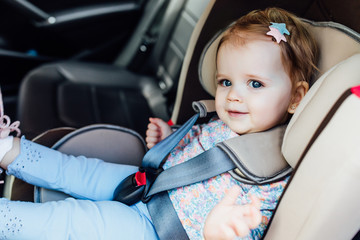 Pretty small child, girl sits in the automobile armchair, fastened by seat belts.