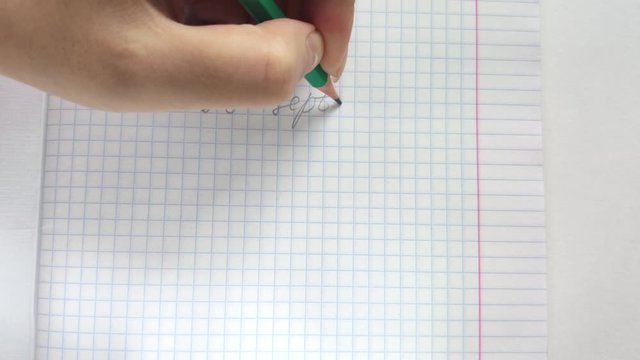 White european woman lefty writes in pencil in a notebook with his left hand the phrase 1st September. Handwritten inscription in pencil on the first of september on squared paper