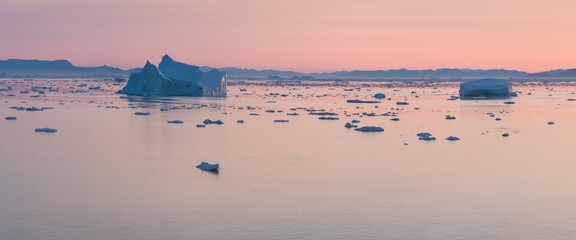 Arctic nature landscape with icebergs in Greenland icefjord with midnight sun sunset / sunrise in...