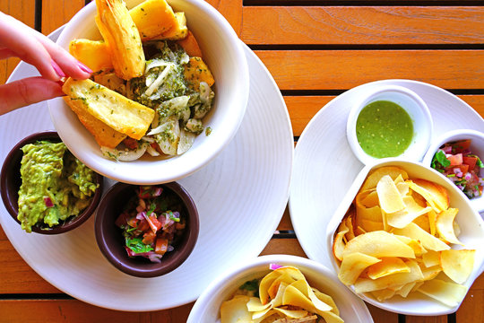 Dipping Yucca Fries With Parsley And Garlic Sauce In Side Dishes Of Guacamole And Salsa