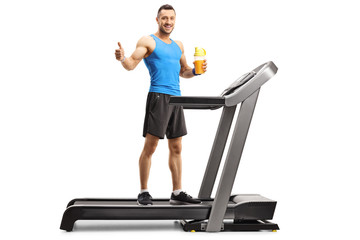 Young fit man on a treadmill holding a cup of sports energy drink and showing thumb up