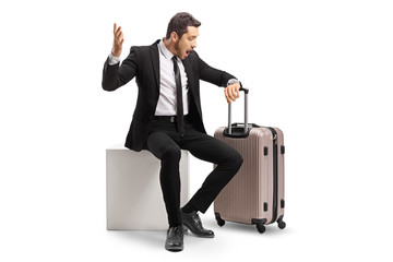 Businessman in panic sitting with a suitcase and looking at his watch