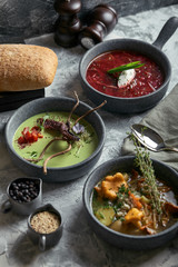 Gray plates with different soups on a gray background. Plate with asparagus soup with octopus, a plate of traditional borscht with sour cream, a plate with mushroom soup and standing on multi-colored