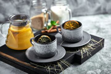 Transparent glass teapot with chitrus tea and cups, tea set on a wooden table. Close up, gray background, soft light.