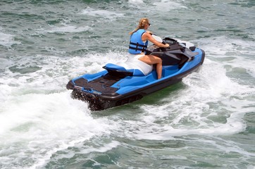 Young blonde woman riding a blue jetski