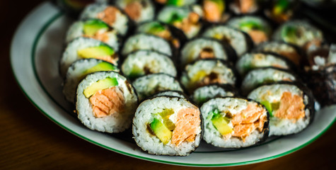  A white plate full of sushi futomaki with baked salmon, kanpyo, marinated radish, avocado and cream cheese