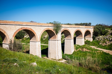 Fototapeta na wymiar Beautiful old stone bridge of abandoned railway crossing a small river. Puglia region, Italy