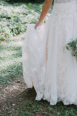 Bride holding wedding dress and flowers, white lace gown