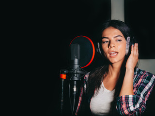 Stock video Young beautiful brunette woman recording voice, song or album in professional studio. Girl sings near microphone in recording room under natural light. 