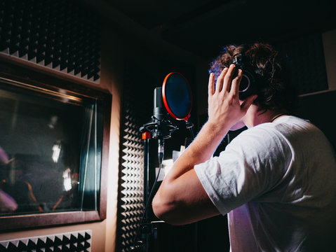 Young handsome singer man puts on headphones in the studio. Recording new melody or album. Male vocal artist with curly hair preparing for working. 