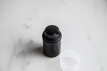 Black cosmetic bottle on light marble background