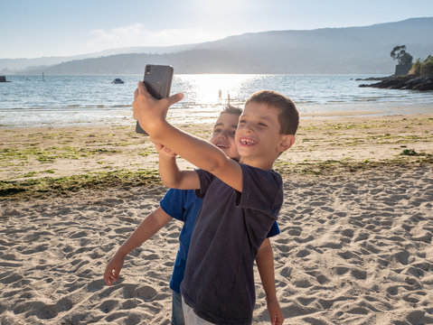 two young children taking a selfie with a mobile phone on the beach looking very happy