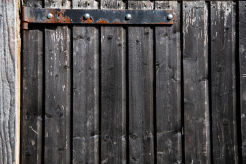 Background brown weathered wooden gate with vertical planks and black painted rusty hinge at top