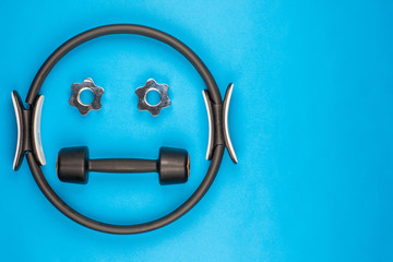 A smiley face made from gym equipment, on blue background, shot from above.