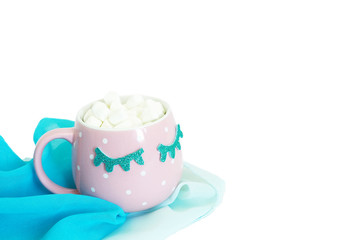 A pink and white polka-dot mug with closed blue eyes with coffee and marshmallows stands on a blue chiffon shawl. Isolate on a white background..