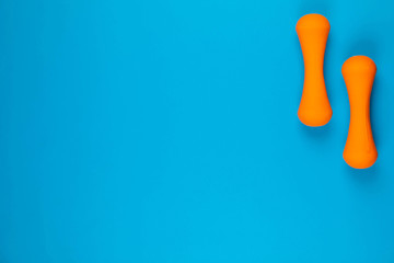 Two dumbbells on blue background, shot from above, aligned at the top right.