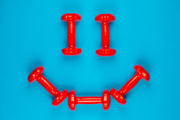 A smiley face made from red dumbbells on blue background, shot from above.