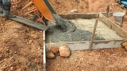 Worker pouring the mixed cement onto the ground for making the foundation of structure