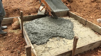 Worker pouring the mixed cement onto the ground for making the foundation of structure