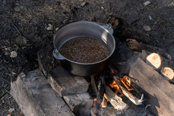 Buckwheat in a cauldron is prepared on a campfire on a sunny summer morning in the forest. Top-side view. 