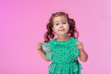 Funny little kid, toddler girl in fashionable green dress isolated on pink background