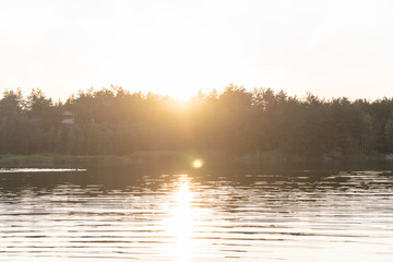 Fototapeta premium View of the water in the ripples in the quarry, on the silhouette of the forest on the opposite bank. Summer orange sunset. 