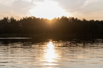 Obraz premium Picturesque landscape. Summer evening at orange sunset - view of the water in the ripples in the quarry, on the silhouette of the forest on the opposite bank. 