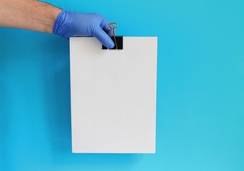 Doctor's hand in glove holding sheets of paper with clip with blank sheet of paper as a sign providing copy space for a message.