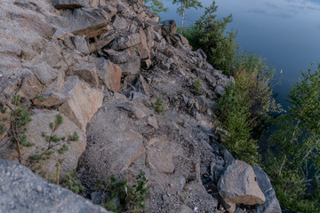 Scenic view of the stones of granite quarry filled with water, and the opposite rocky shoreovergrown with trees after sunset at dusk in the summer. 