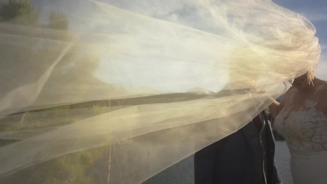 A bride's veil flows across the frame at an outdoor wedding in the evening