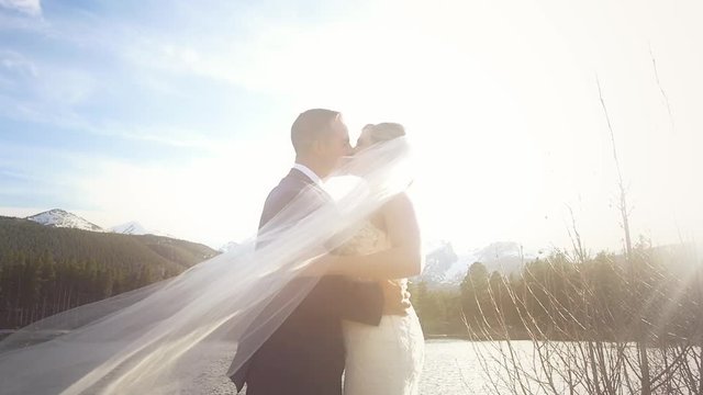 Bride and groom kiss in the mountains as her veil blows across the frame