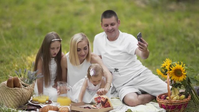 Family picnic time in nature, father tries to take picture with smartphone while his young restless daughter playing with pieces of pizza