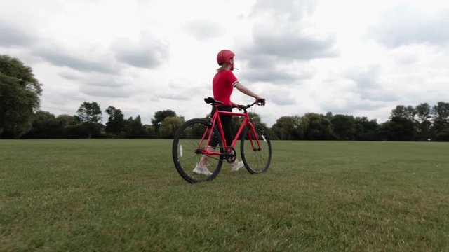 Caucasian female cyclist in red top walking with her bike in a park in slow motion
