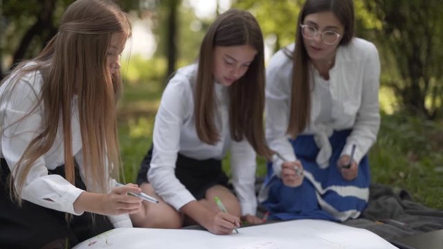 Schoolgirls working together writing on large piece of paper in park