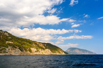 Fototapeta na wymiar Ayu-Dag mountain from the side of a pleasure boat in the black sea, on a sunny day with clouds in the sky.
