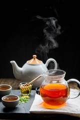 Hot tea in a teapot and teacup with steam on revive the wood and a black background.